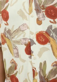 Cămașă cu nasturi, având un fundal crem și modele colorate de fructe și legume, inclusiv roșii roșii și frunze verzi, cu nasturi.