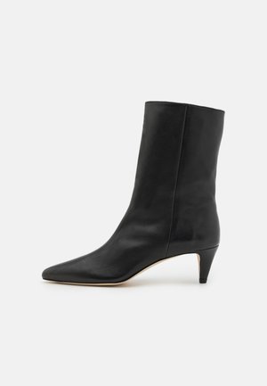 Bottine en cuir noir avec un bout pointu, un talon conique de hauteur intermédiaire, une texture lisse et un design minimaliste.