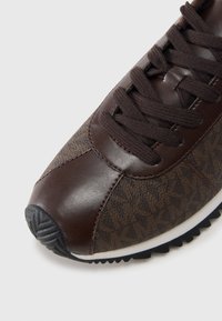 Brun skinn- og mønstret stoff-sneaker med mørke snøringer, rund tå og teksturert gummisåle. Fremhevet med kontrasterende søm.