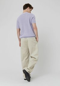 Polo shirt en tricot lilas clair, pantalons baggy beiges et baskets noires. Texture douce, manches courtes et détails de poche arrière visibles.