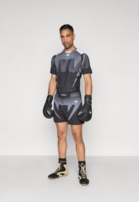 Conjunto atlético preto e cinzento com mangas curtas e calções, apresentando padrões geométricos. Luvas de boxe pretas e calçado com detalhes em castanho claro.