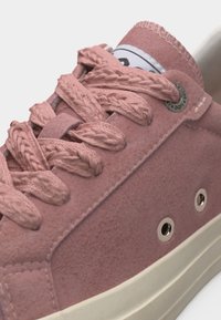 Κοντινό πλάνο σε ροζ σουέντ αθλητικό παπούτσι με παχιά πλεκτά κορδόνια, μεταλλικά οπές και λευκή λαστιχένια σόλα.