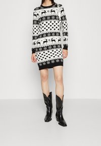 Robe en tricot noire et blanche avec un motif festif comprenant des rennes, des cœurs et des flocons de neige. Manches longues, poignets côtelés et encolure ronde.