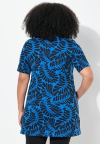 Túnica de manga corta en azul brillante con un patrón de hojas en negro. La tela tiene una textura suave y un corte holgado, con un dobladillo curvado.