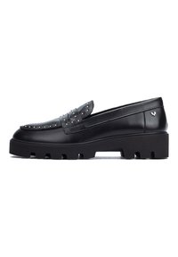 Mocasines de cuero negro con acentos de tachuelas, una suela de plataforma gruesa y una textura suave. Presenta un detalle de lazo decorativo en la parte frontal.
