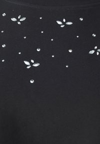 Tissu noir décoré de petits strass clairs dispersés et en grappes formant des motifs floraux près de l'encolure.