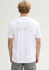 Witte katoenen T-shirt met op de achterkant in grijs en rood bedrukte tekst, met een losse pasvorm en korte mouwen.