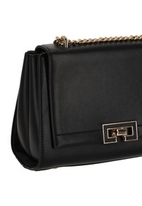 Bolso de mano de cuero negro con correa de cadena dorada y cierre decorativo rectangular en la solapa frontal, mostrado desde un ángulo lateral sobre fondo blanco.