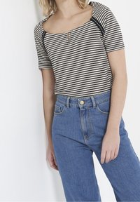 Haut en maille rayé à manches courtes, décolleté carré avec détail œillet, associé à un jean en denim bleu taille haute.