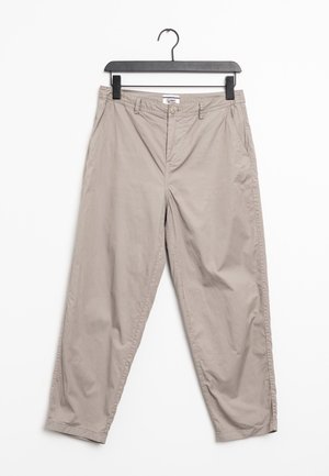 Pantalones chinos beige de algodón, con cierre de botón, bolsillos laterales y un corte relajado. Colgados de una percha de plástico negra.
