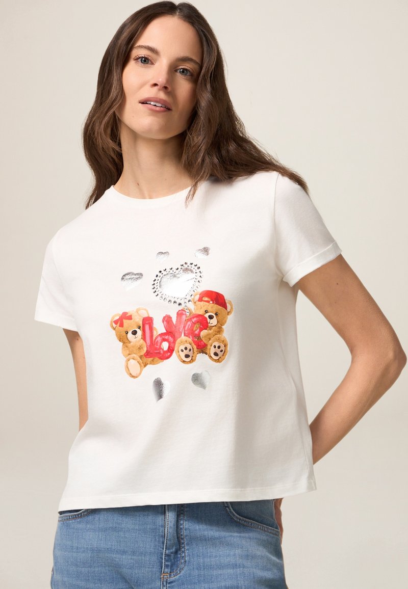 Weißes Baumwoll-T-Shirt mit einem gestickten Design von zwei Teddybären und dem Wort "Liebe" in Rot, akzentuiert mit silbernen Herzen.