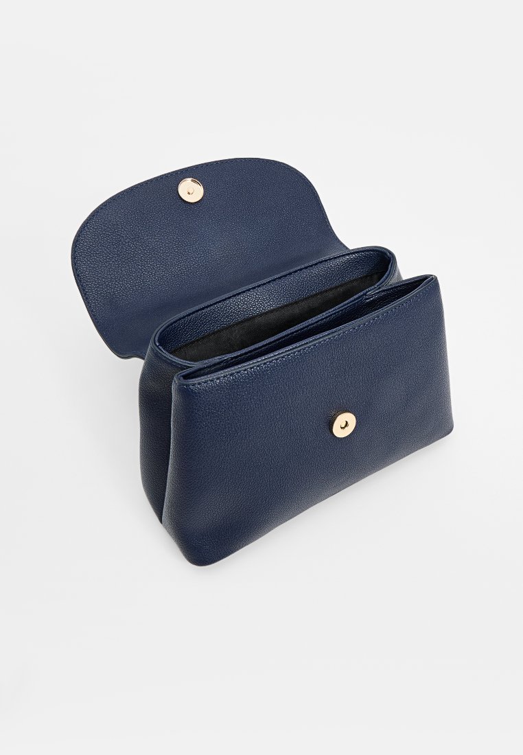 Sac à main en cuir bleu marine avec une finition texturée, une fermeture à bouton magnétique et un intérieur spacieux. Design ouvert montrant un compartiment principal.