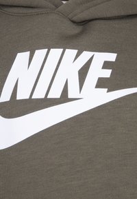 Capuche vert olive avec un grand logo blanc "NIKE" et un graphique de swoosh sur le devant. Le tissu a une texture lisse.