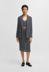 Marineblauw textuur twee-delig set met een cropped top met een V-hals en een bijpassende rok tot de knie. Gecombineerd met zwarte instappers.