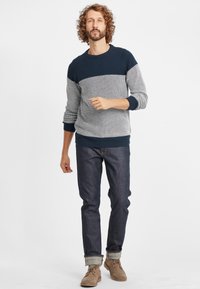 Maglione lavorato a maglia con blocchi di colore blu navy e grigio chiaro, motivo a texture, polsini e orlo a costine, abbinato a jeans scuri e scarpe marrone chiaro.