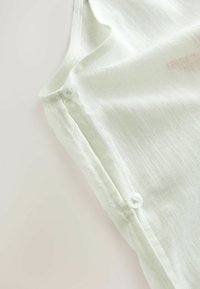 Tissu blanc semi-transparent avec deux petits boutons blancs cousus le long d'une couture, gros plan sur la texture lisse et légère du textile.