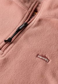Pullover in pile rosa chiaro con mezza cerniera, dotato di cordoncino nero e logo "superdry" ricamato in bordeaux. Texture morbida.