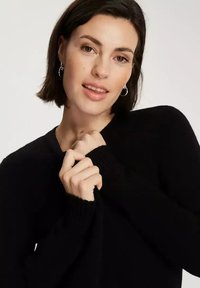 Czarny sweter z miękkiego materiału, z głębokim dekoltem w serek i ściągaczami przy mankietach. Eksponowany z delikatnie złożonymi rękawami.