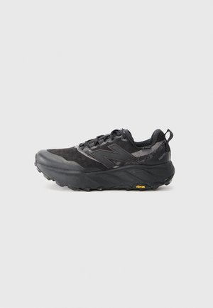 Trail running shoe in black with textured upper and synthetic material. Features a Vibram outsole and reinforced toe cap. Light cushioning visible.