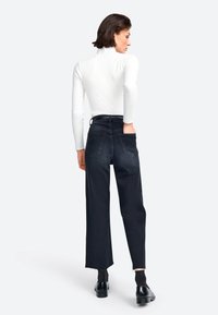 Schwarze, weit geschnittene Jeanshose mit hoher Taille, fransigem Saum und zwei Gesäßtaschen, getragen mit einem figurbetonten, weißen, gerippten Rollkragenoberteil.