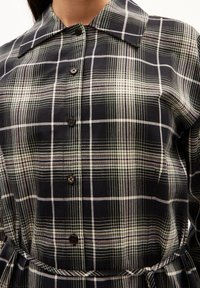 Abito a quadri neri con scollatura a colletto, chiusura con bottoni e vita cintrata. Tessuto testurizzato con linee verdi e bianche.