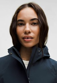 Jachetă waterproof navy cu guler înalt, fermoar complet și închidere cu capse. Textură netedă, design minimalist, fără modele sau logo-uri vizibile.