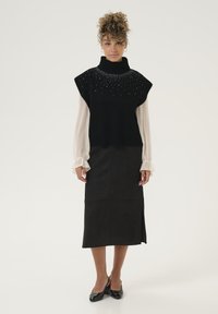 Črna pletena brezrokavnica z visokim ovratnikom in okrasnimi kamni, v kombinaciji s črnim semiskratkim krilom in črnimi petkami.