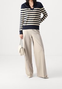 Sweter w paski w kolorze granatowym i kremowym z dekoltem w serek, szerokie beżowe spodnie oraz jasnokremowa torebka na łańcuszku. Gładka tkanina i dopasowany krój.
