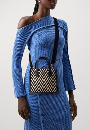 Sac à main tissé à motif chevron noir et beige avec deux poignées et une bandoulière amovible, assorti à une robe bleue côtelée texturée.
