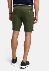 Groene casual shorts met een rechte snit, twee achterzakken met knopen en een tailleband met een gestreept ontwerp. Gedragen met marineblauwe schoenen.