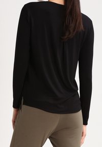 Top negro de manga larga con un corte relajado y escote redondeado, hecho de una tela suave y ligera, combinado con pantalones verdes oliva.