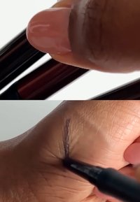 Black felt-tip pen held by a hand, drawing a line on skin. The pen has a glossy, dark casing and a pointed tip; skin shows texture and creases.