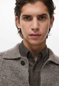 Abrigo de mezcla de lana gris para hombre con cuello de muesca, cierre de botones, y una camisa oscura de botones debajo, con una textura suave.
