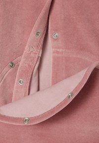 Rosa Cordstoff mit weicher Textur, versehen mit silbernen Druckknöpfen und einem leichten Futter. Detaillierte Nähte sind sichtbar.