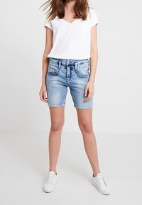 Jasnoniebieskie szorty dżinsowe o klasycznym kroju, z pięcioma kieszeniami i delikatnym przetarciem na końcu. W zestawie z białą koszulką z dekoltem w serek.