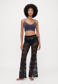Pantaloni a zampa nera in pizzo con motivi floreali e una texture trasparente abbinati a un top corto blu scuro con spalline sottili.