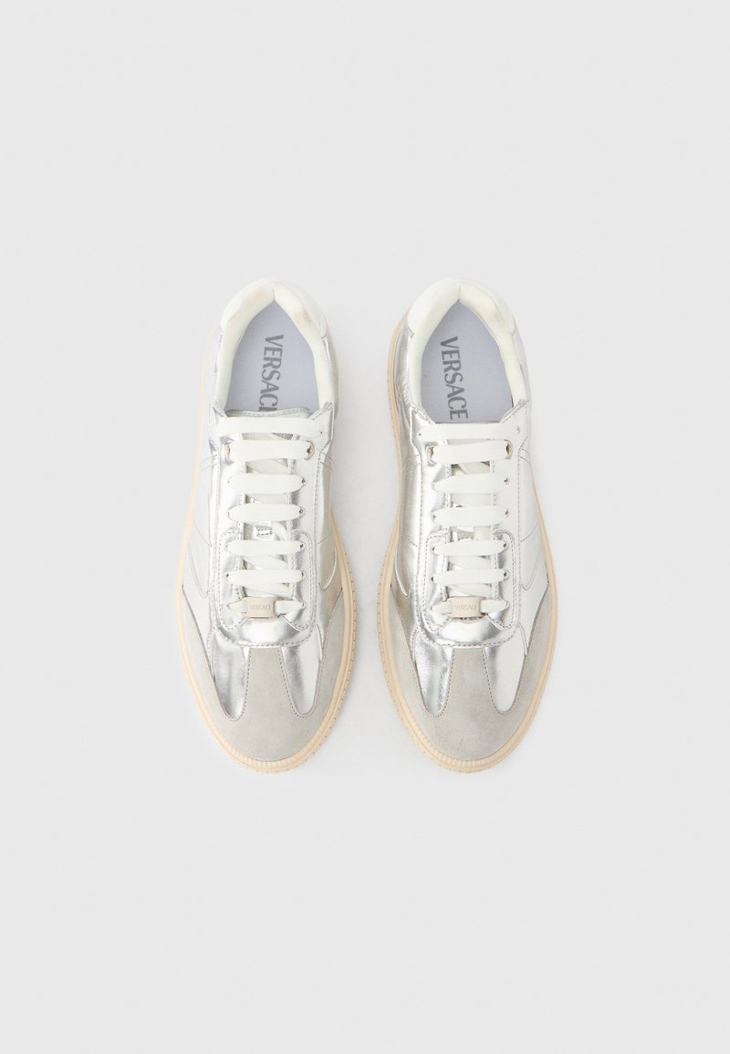 Sneakers argento con una combinazione di materiali metallici e in suede, con lacci bianchi, suola in gomma color cuoio e design con punta rotonda. Branding Versace sulla soletta.