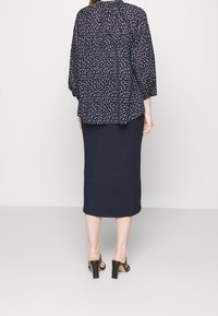 Blusa floreale blu navy con una vestibilità ampia e maniche lunghe, abbinata a una gonna midi a costine blu navy. La persona indossa mule con tacco neri.