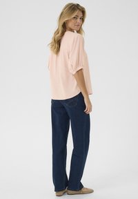 Blusa rosa chiaro a maniche corte con vestibilità rilassata, scollatura rotonda e polsini abbottonati, abbinata a jeans dritti blu scuro.