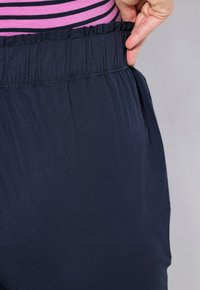 Marinblå byxor med elastisk midja, detaljerad med en samlad midja och slät yta, visad i kombination med en rosa och randig topp.