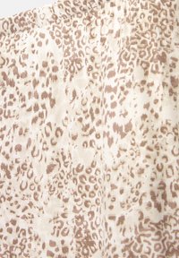 Tissu beige clair avec un motif léopard marron doux et de légers plis créant une texture sur la surface.