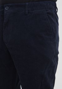 Pantaloni in corduroy blu navy con una finitura testurizzata, caratterizzati da una chiusura con un unico bottone, tasche laterali e un design a gamba affusolata.