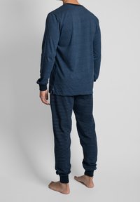 Marineblauw pyjamashirt met lange mouwen en ronde hals; gecombineerd met gestreepte pyjamabroek. Zachte, gestructureerde stof. Manchetten aan mouwen en enkels.
