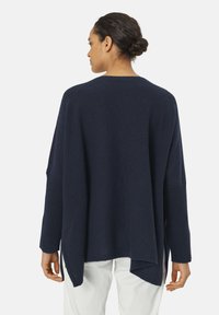Marineblaues, übergroßes Sweatshirt mit weitem Halsausschnitt, überschnittenen Schultern und seitlichen Schlitzen. Hergestellt aus einem weichen, strukturierten Strickstoff.