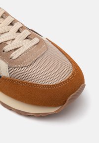 Sneaker bej din materiale mesh și suede. Vârf rotund, accente texturate de culoare maronie și șireturi bej. Talpa din cauciuc prezintă riduri subtile.