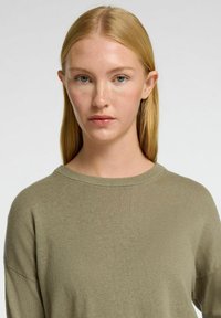 Olivgrüner Strickpullover mit weitem Halsausschnitt und langen Ärmeln, der eine weiche Textur und eine lockere Passform bietet, ideal für legere Anlässe.