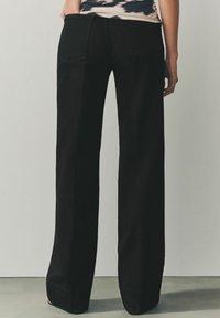 Schwarze, weit geschnittene Jeans mit hoher Taille, die ein sauberes Design und minimale Nähte aufweist. Der Stoff wirkt robust, mit subtil ausgefellten Säumen.
