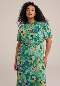 Robe florale avec une base verte, décorée de fleurs jaunes et violettes. Elle a des manches courtes, une taille cintrée et un design plissé.