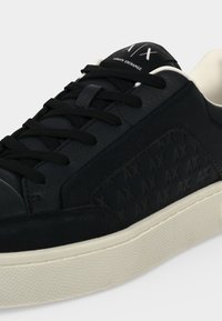 Черна маратонка Armani Exchange с черни връзки, релефен модел AX отстрани и бели подметки и детайли на вътрешната облицовка.