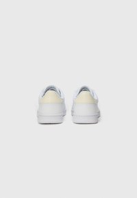 Hvite sneakers med en glatt lær-overdel, som har en lys kremfarget bakpanel, rund tå og hvit gummisåle. Minimalistisk design.
